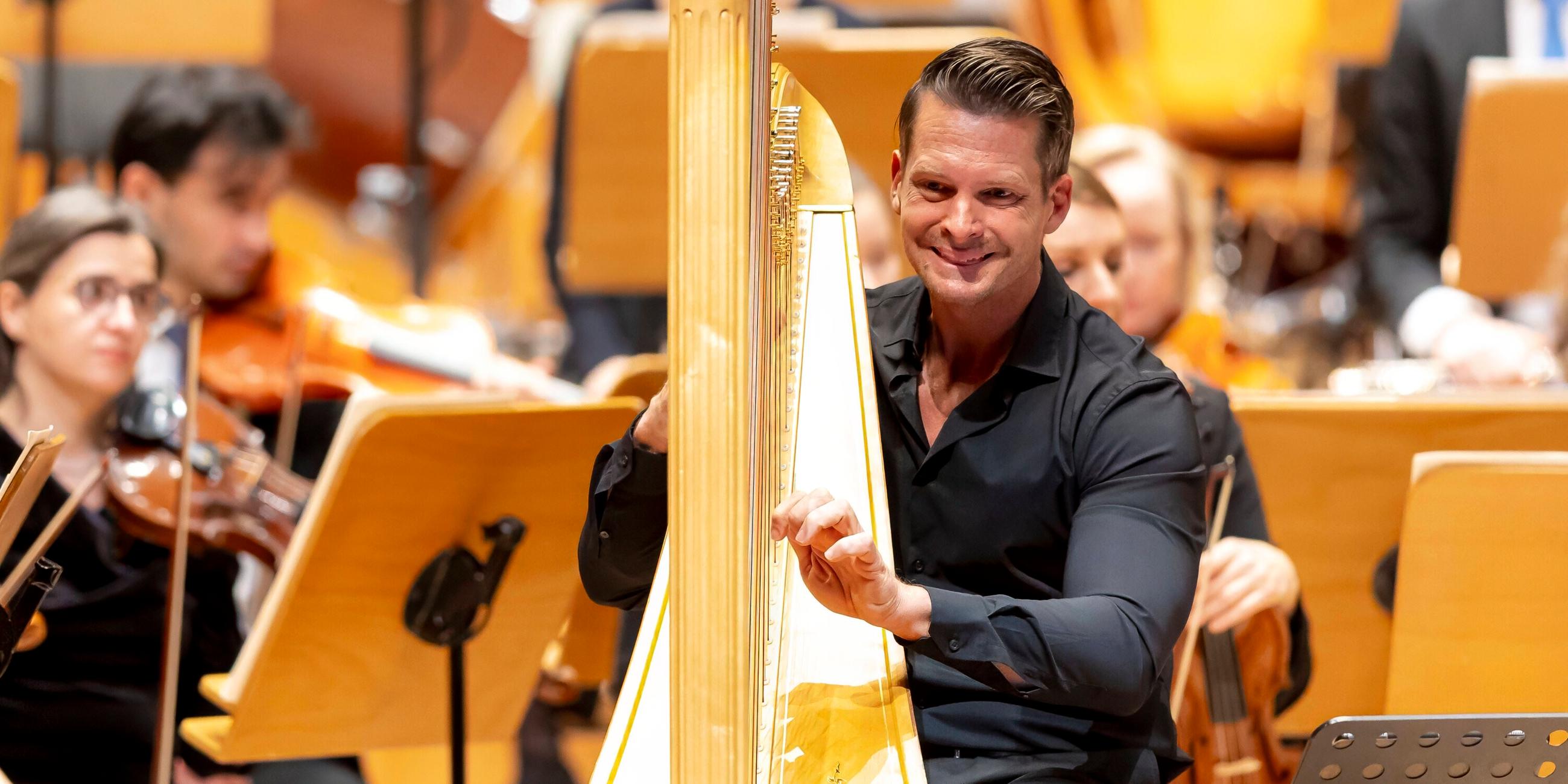 Ein Mann spielt auf einer Harfe, umgeben von einem Orchester.