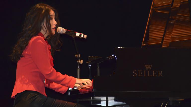 Eine Frau, die eine rote Bluse trägt, sitzt an einem Flügel und singt.