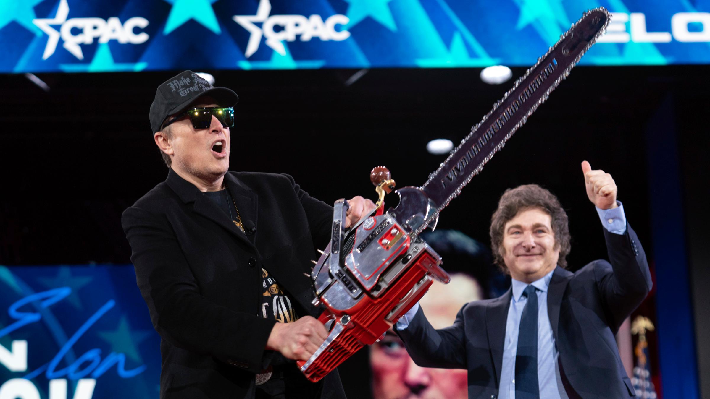 Elon Musk hält eine Kettensäge hoch, die er vom argentinischen Präsidenten Javier Milei (rechts) erhalten hat, als sie am 20. Februar 2025 im Gaylord National Resort & Convention Center in Oxon Hill, Maryland, zu ihrer Rede auf der Conservative Political Action Conference (CPAC) eintreffen. 