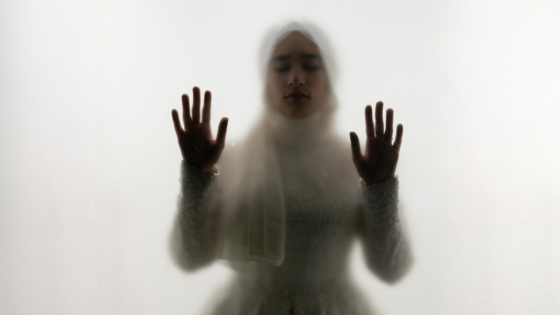 Muslimische Frau steht hinter Glas