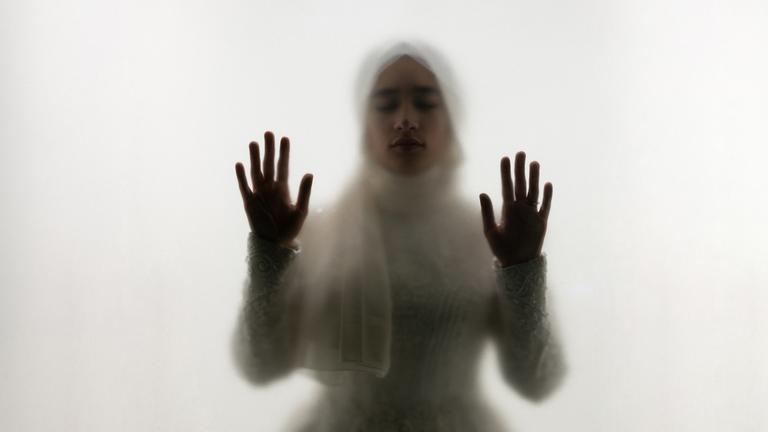 Muslimische Frau steht hinter Glas