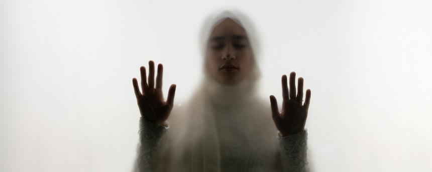 Muslimische Frau steht hinter Glas