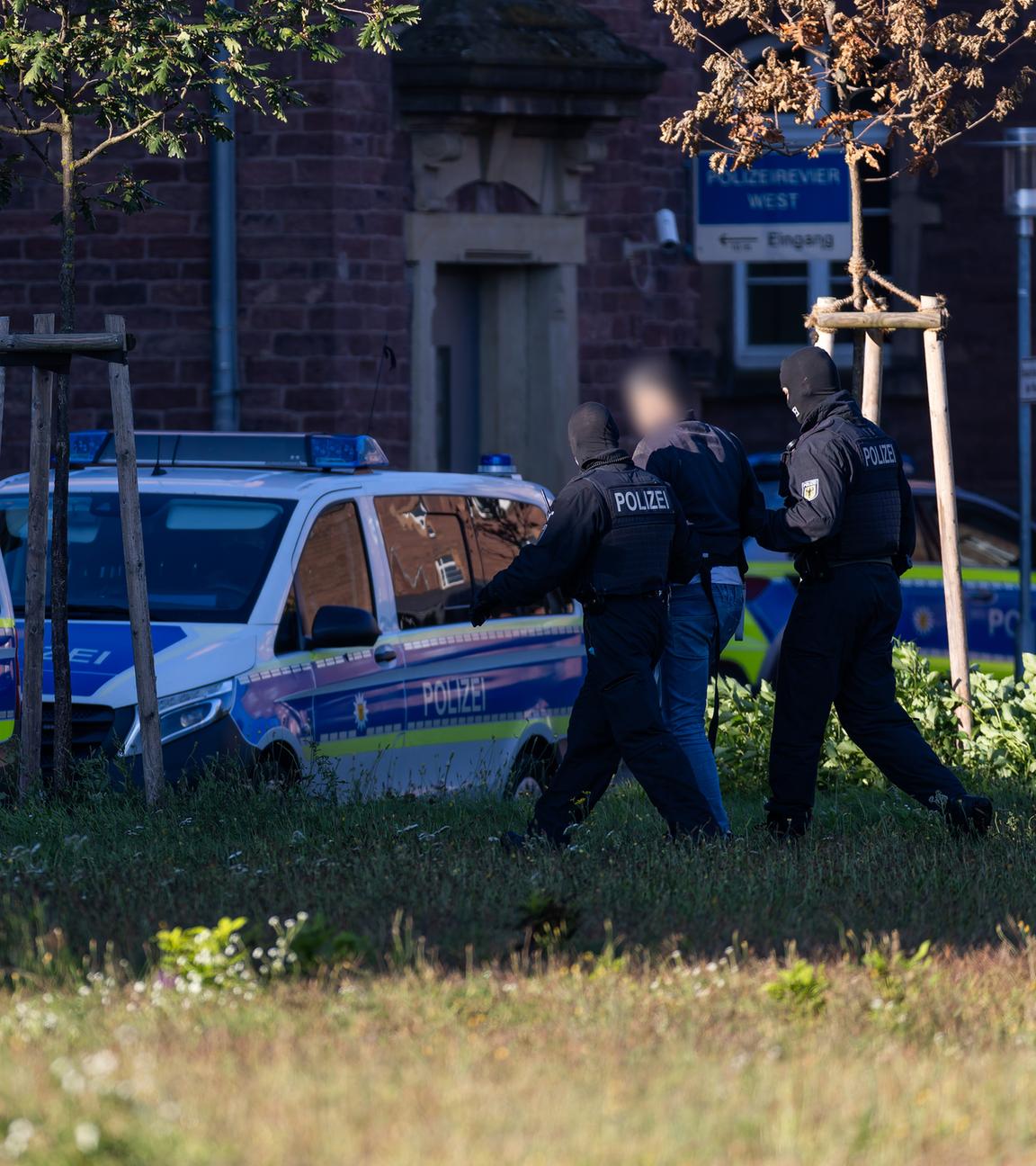 Ein Mann wird von zwei Bundespolizisten zu zwei wartenden Einsatzfahrzeugen geführt.