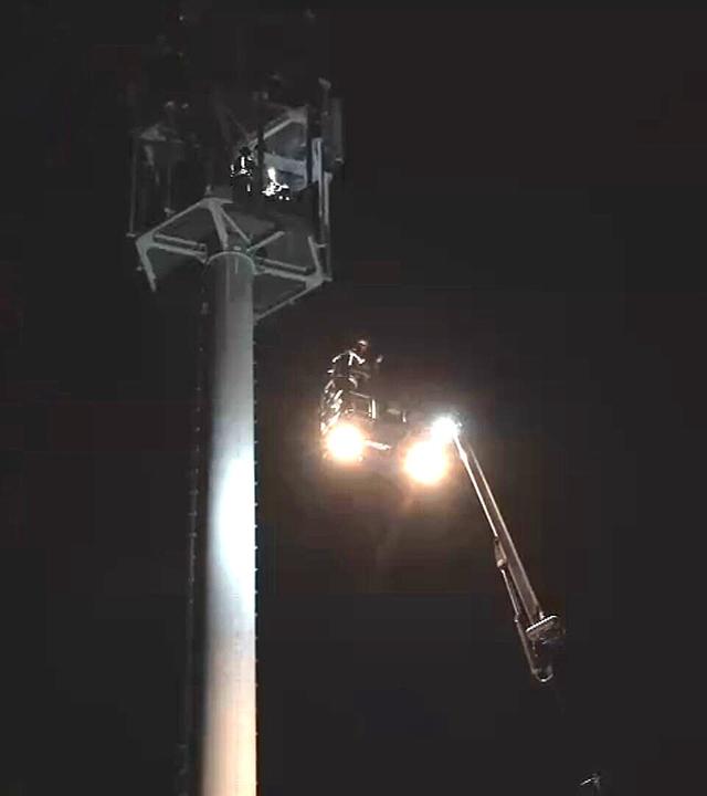 Die Feuerwehr fährt mit einem Kran an einen Funkmast ran. Es ist dunkel. 