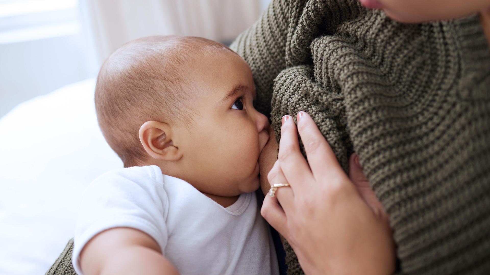 Eine junge Frau stillt ihr Baby zu Hause auf dem Sofa.