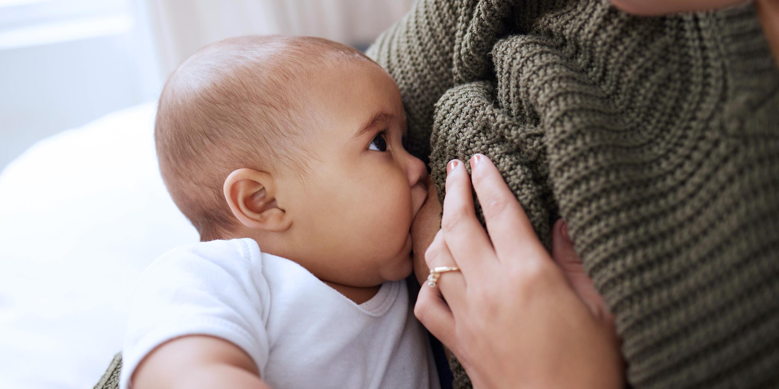 Eine junge Frau stillt ihr Baby zu Hause auf dem Sofa.
