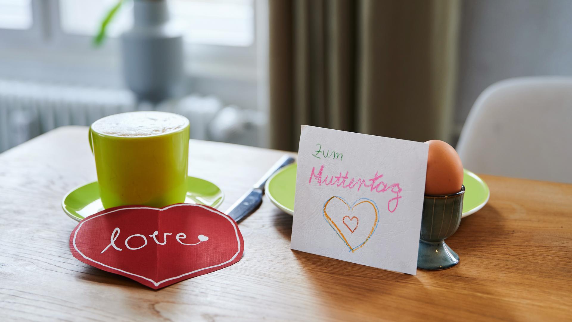 "Zum Muttertag" und "love" steht auf selbst-gebastelten Karten, die auf dem Frühstücksgedeck liegen.