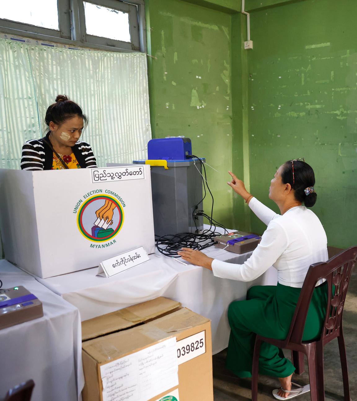Wähler warten vor der Wahlkabine in einem Wahllokal mit grünen Wänden in Myanmar.