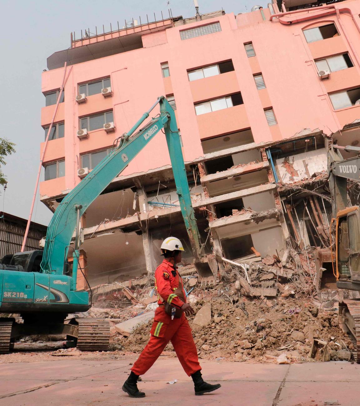 Ein Bergungsretter läuft in Mandalay in Myanmar an zwei Baggern vorbei, die nach dem Erdbeben Trümmer von einem eingestürzten Gebäude entfernen.