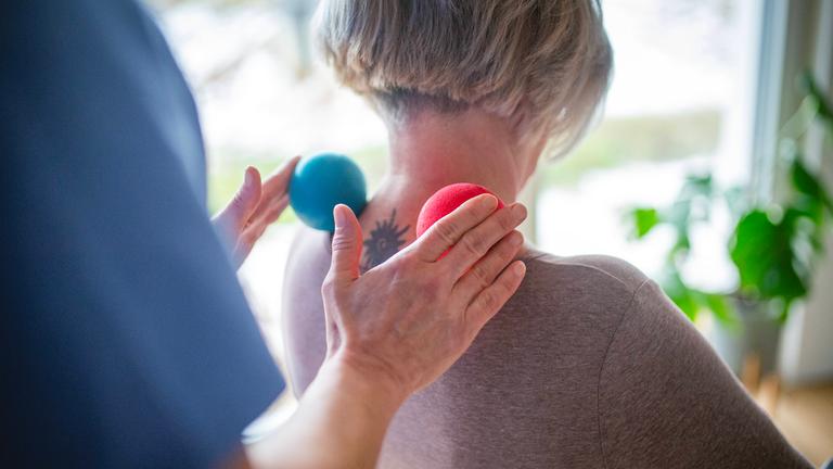 Physiotherapeutin hilft einer älteren Frau bei einer Nackenübung mit Massagebällen.