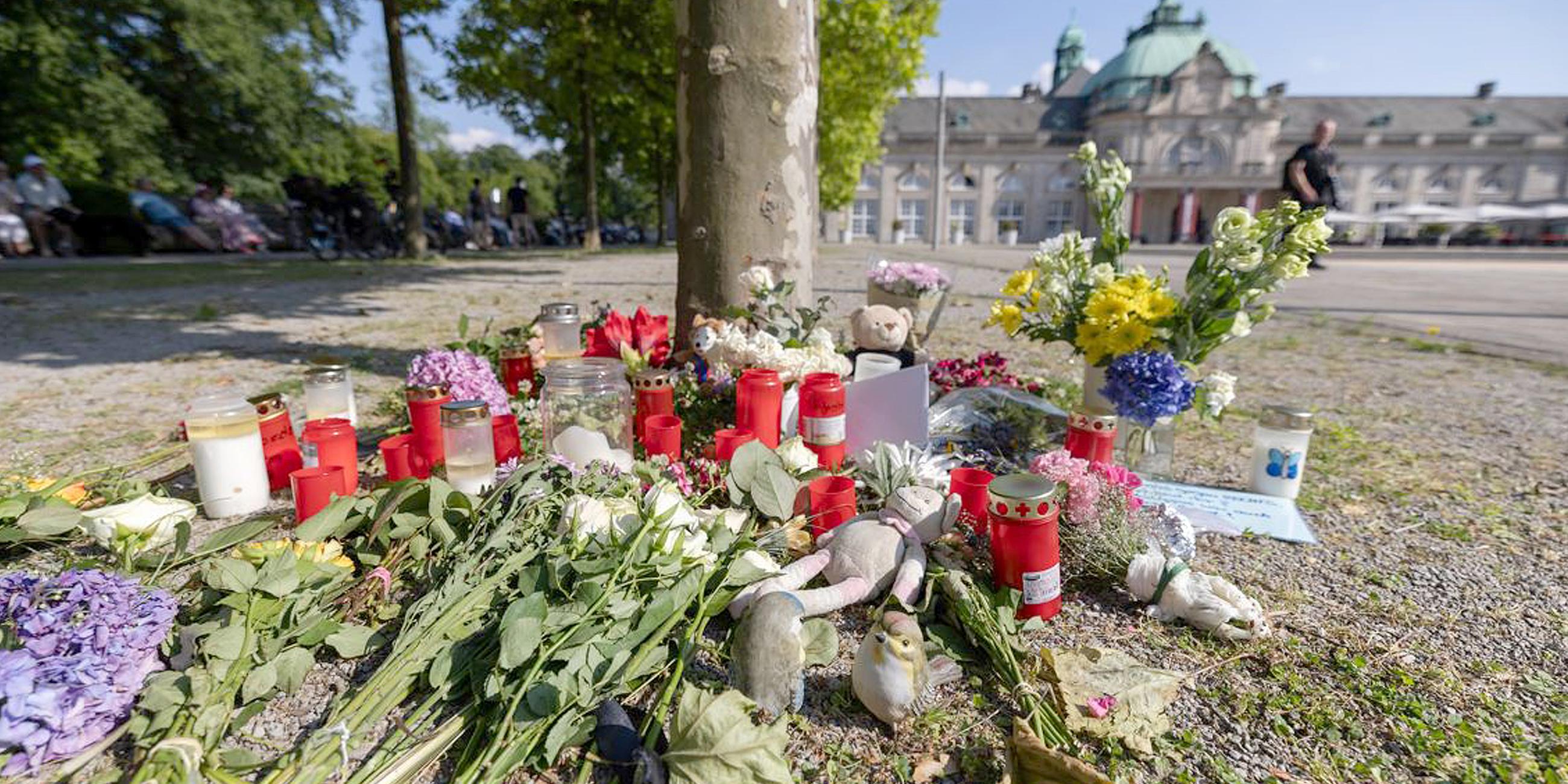 Blumen, Kerzen und handgeschriebene Trauerbekundungen stehen an einem Baum im Kurpark Bad Oeynhausen.