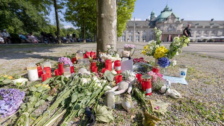 Blumen, Kerzen und handgeschriebene Trauerbekundungen stehen an einem Baum im Kurpark Bad Oeynhausen.
