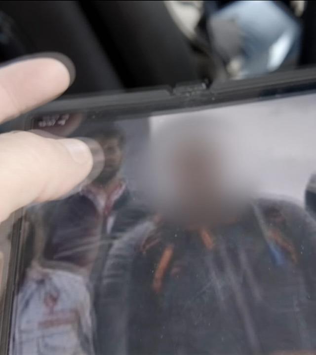 Eine Hand hält ein Tablet, auf dessen Bildschirm drei Männer in Uniformen bzw. Einsatzkleidung zu sehen sind. Einer von ihnen zeigt den aus Lettland stammenden Oleg L, einer der mutmaßlichen Attentäter auf den Flughafen Leipzig/Halle am 4. August 2026.