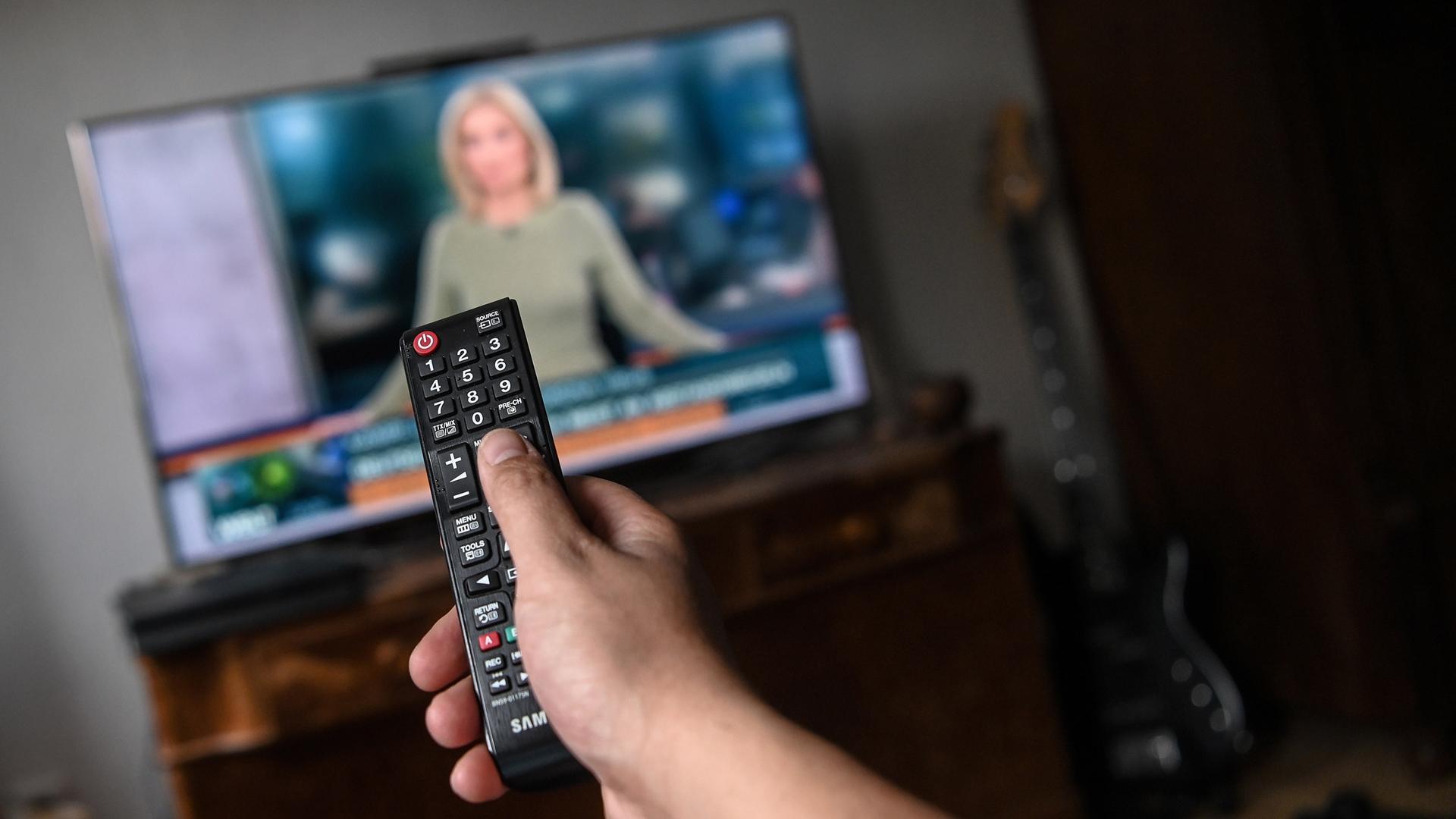 Ein junger Mann sitzt vor dem Fernseher und schaut Nachrichten.