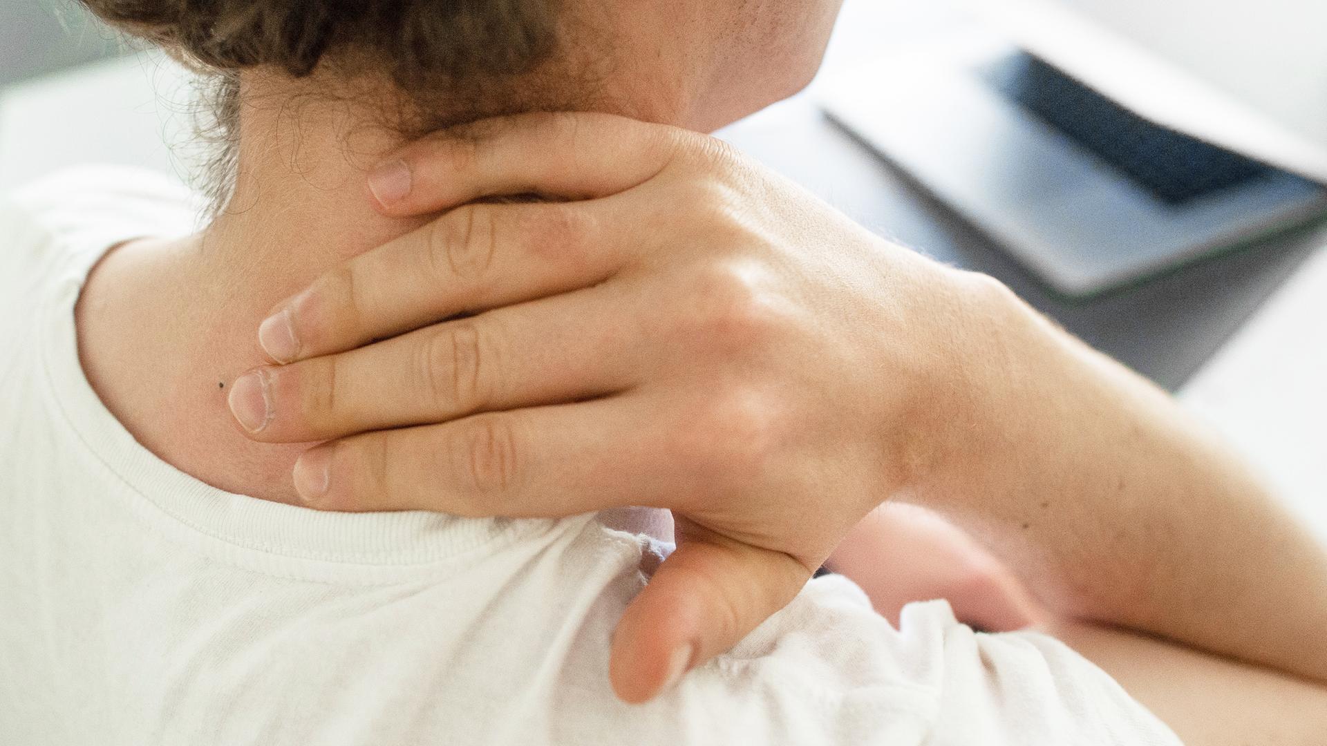 Eine Frau sitzt am Schreibtisch und hält sich die Hand an den Nacken.