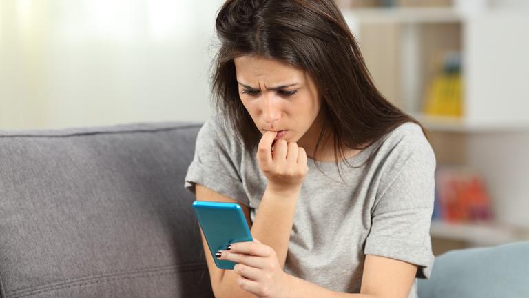 Frau kaut an Nägeln und schaut aufs Handy.