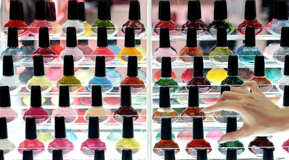 Flaschen mit Nagellack in unterschiedlichen Farben stehen in einem Regal in mehreren Reihen nach hinten in der Höhe aufsteigend präsentiert.