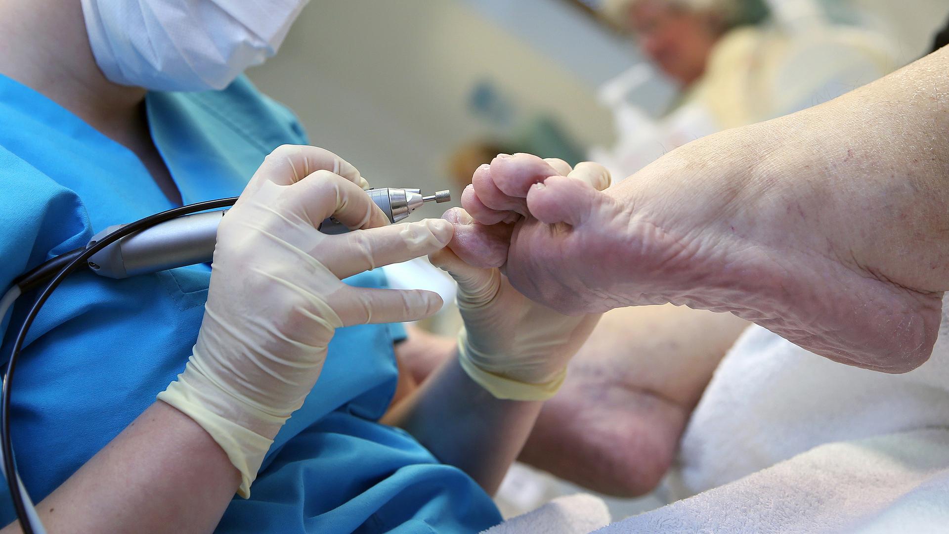Eine medizinisch geschulte Person reinigt die Zehennägel einer Patientin.