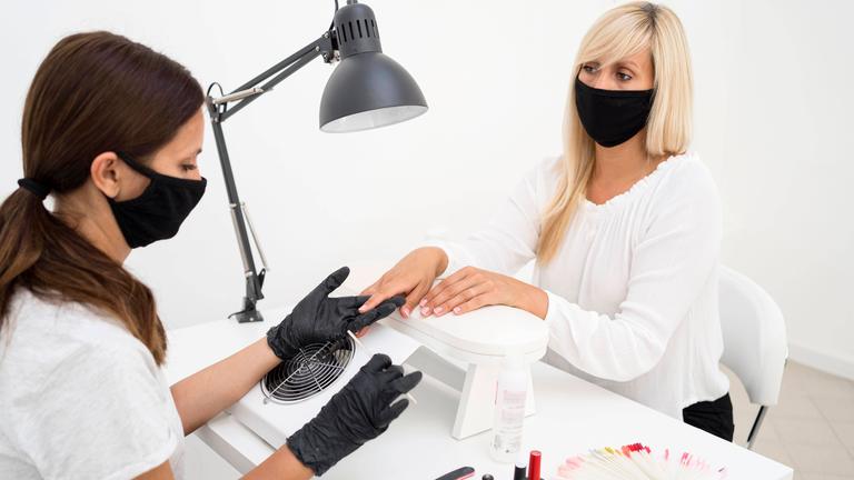 In einem Nagelstudio feilt eine Nageldesignerin einer Kundin die Fingernägel.