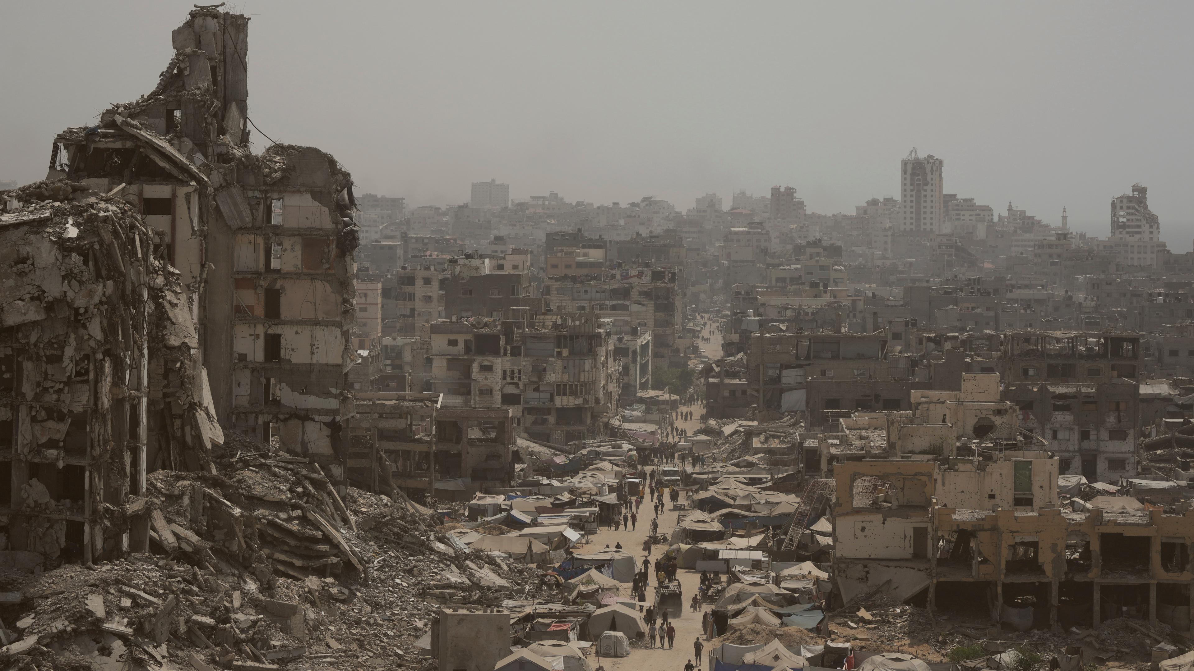 Menschen gehen eine Straße in Gaza-Stadt entlang, die von Gebäuden umgeben ist, die durch israelische Bombardierungen zerstört wurden