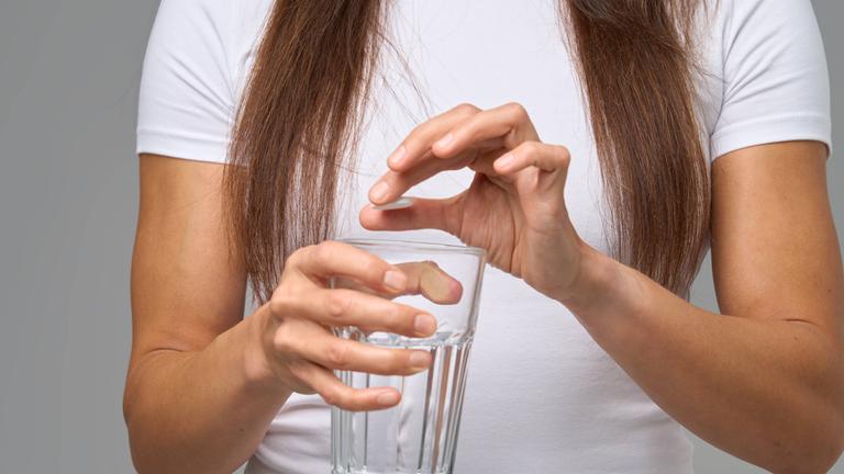 Frau gibt Nahrungsergänzungsmittel in ein Glas Wasser.