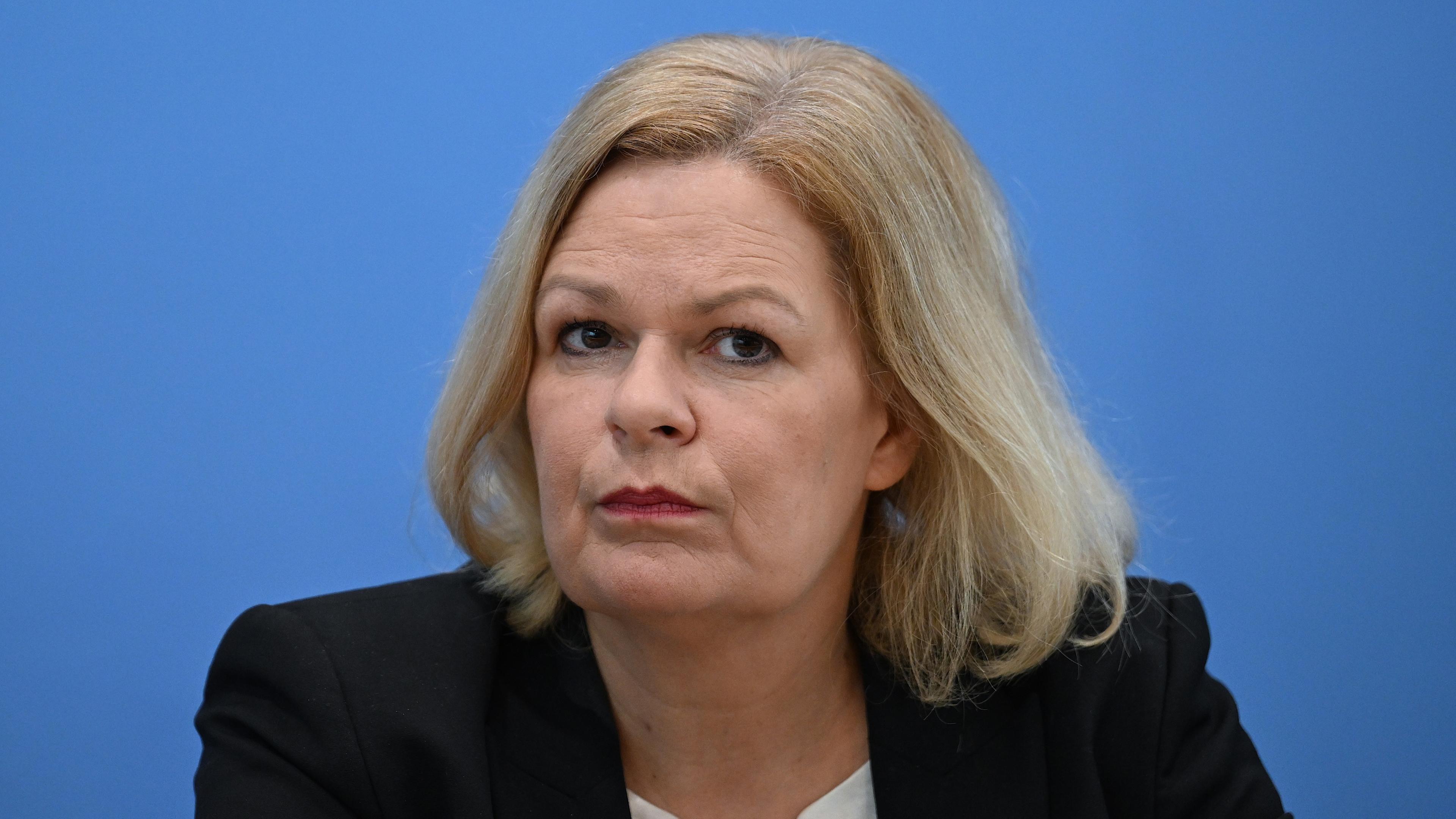 Bundesinnenministerin Nancy Faeser hinter blauer Wand.