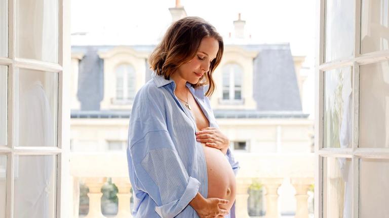 Natalie Portman ist in schwangerem Zustand vor einem Fenster zu sehen.
