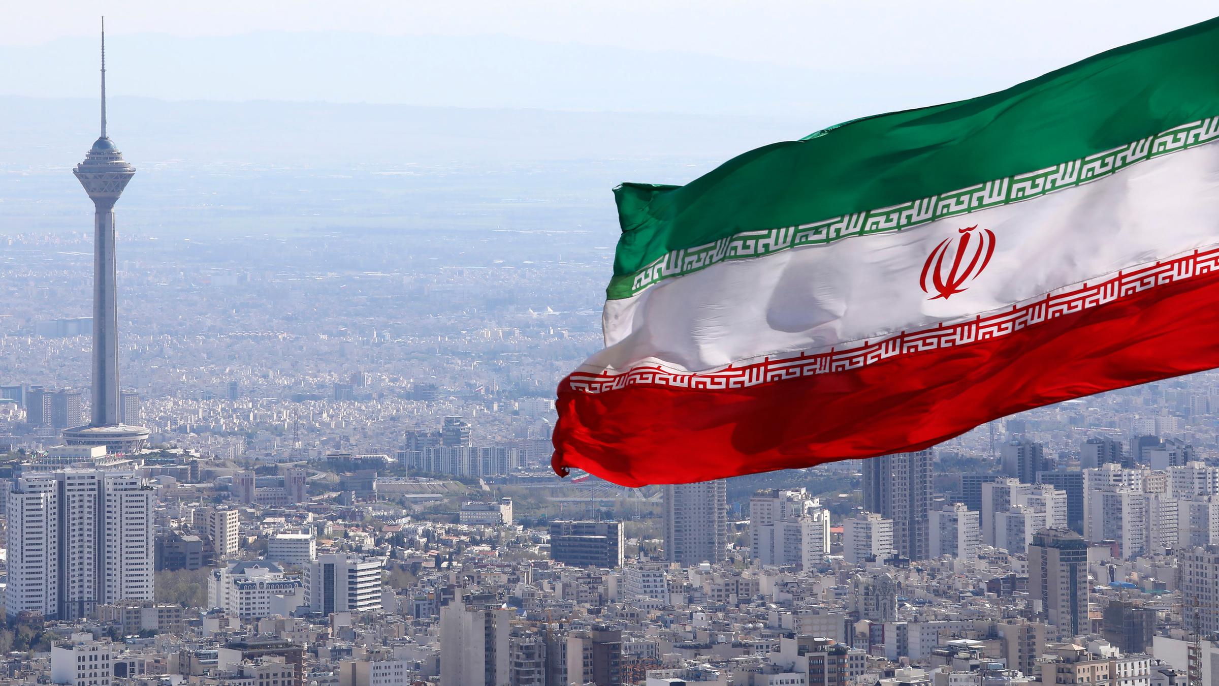 Die iranische Nationalflagge, während der Milad-Telekommunikationsturm und Gebäude in Teheran, Iran, zu sehen sind am 31.03.2020.