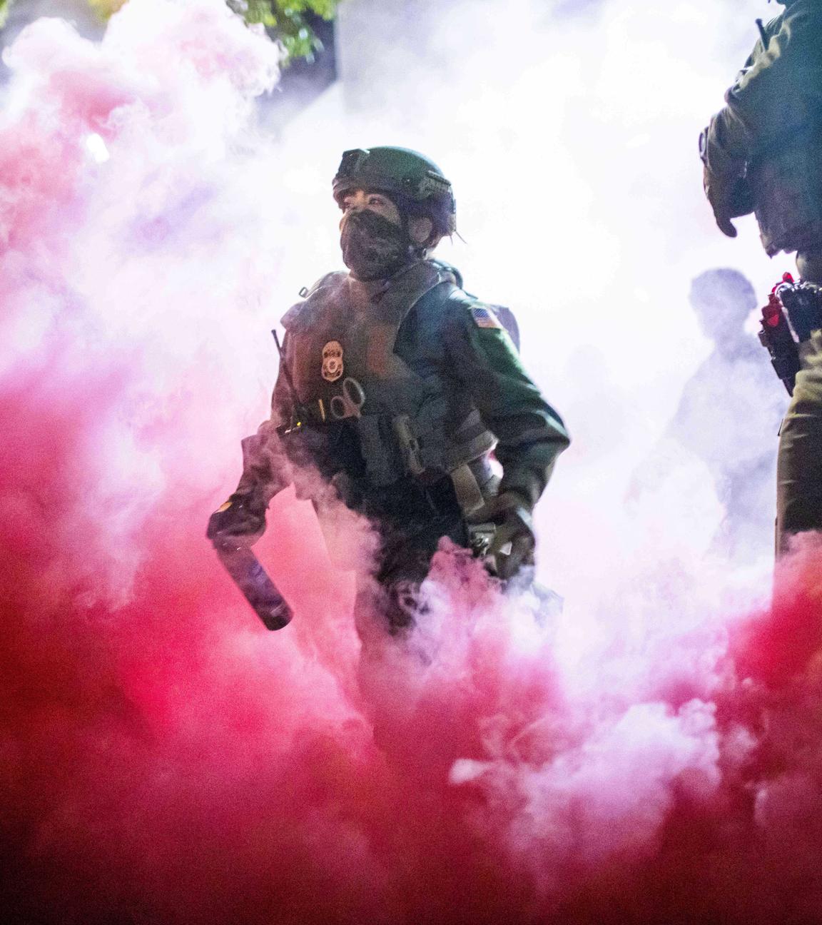  Polizisten und Bundesbeamte werfen Gaskanister, um Demonstranten in der Nähe einer Einrichtung der US-Einwanderungs- und Zollbehörde in Portland zu vertreiben.