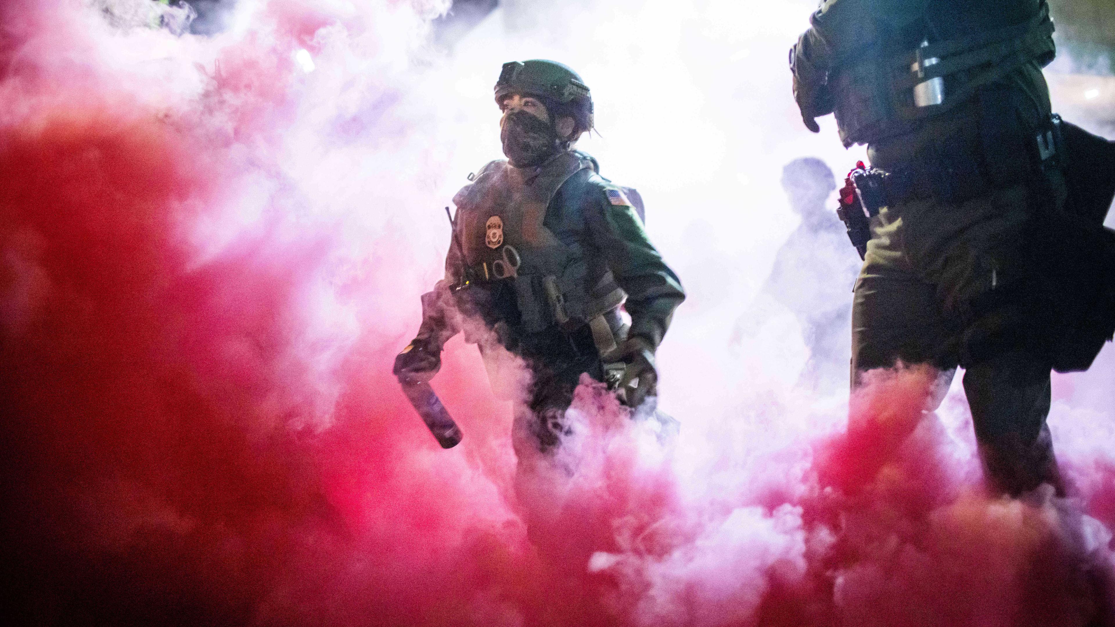  Polizisten und Bundesbeamte werfen Gaskanister, um Demonstranten in der Nähe einer Einrichtung der US-Einwanderungs- und Zollbehörde in Portland zu vertreiben.