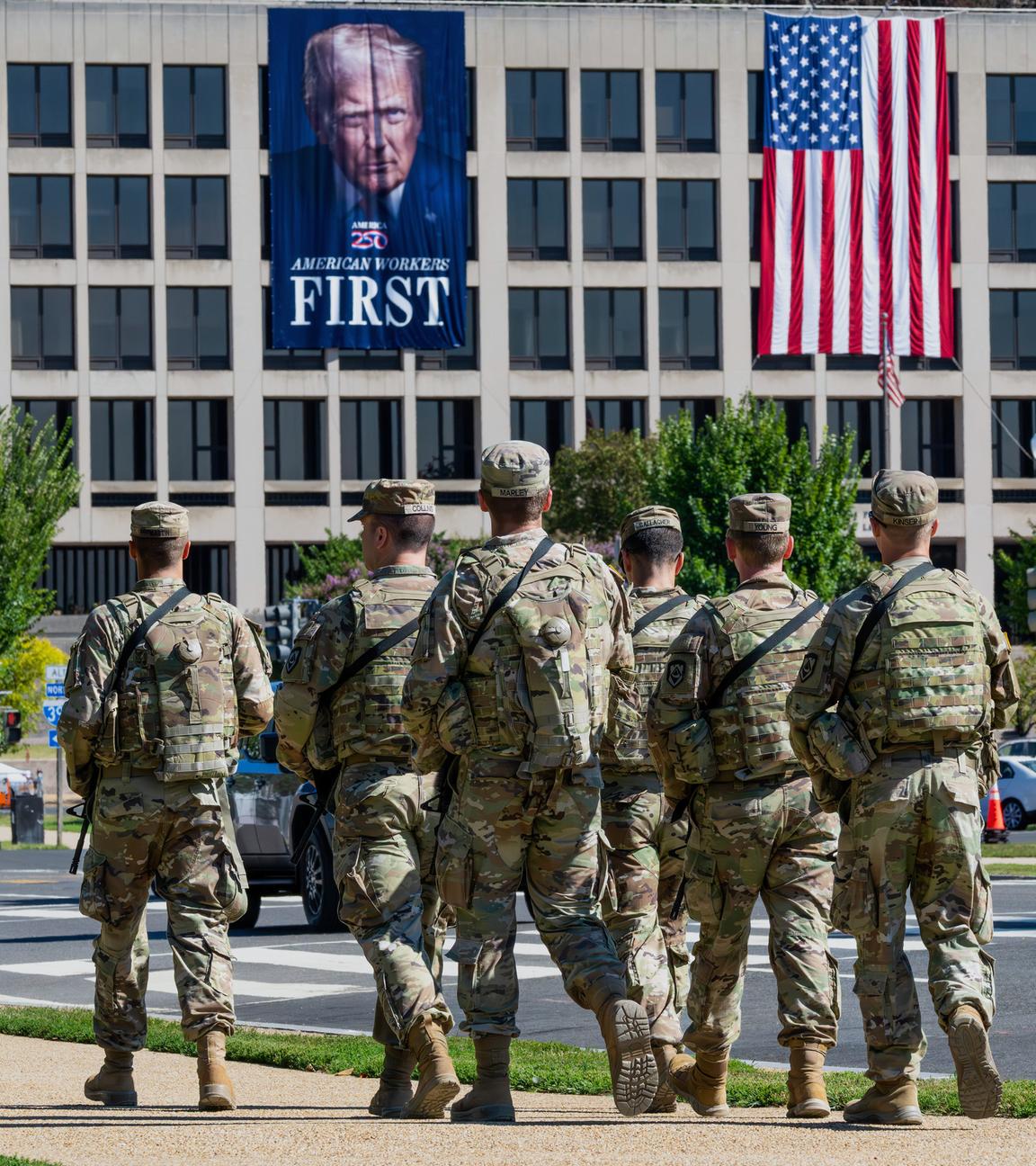 26.08.2025, USA, Washington: Bewaffnete Soldaten der Nationalgarde aus West Virginia patrouillieren auf der Mall in der Nähe des Arbeitsministeriums, wo ein Banner von US-Präsident Trump hängt.
