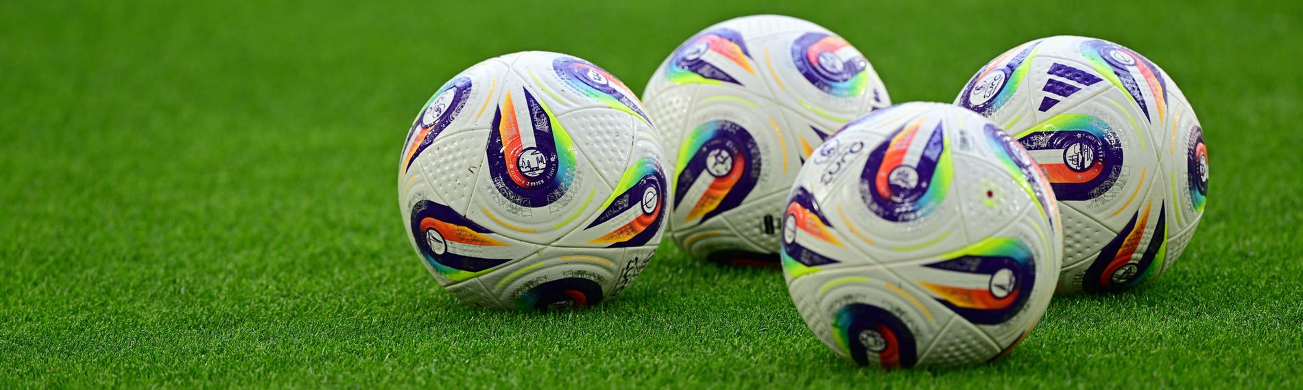 Vier Fussballbälle liegen auf dem Rasen.
