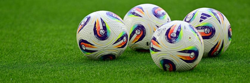 Vier Fussballbälle liegen auf dem Rasen.