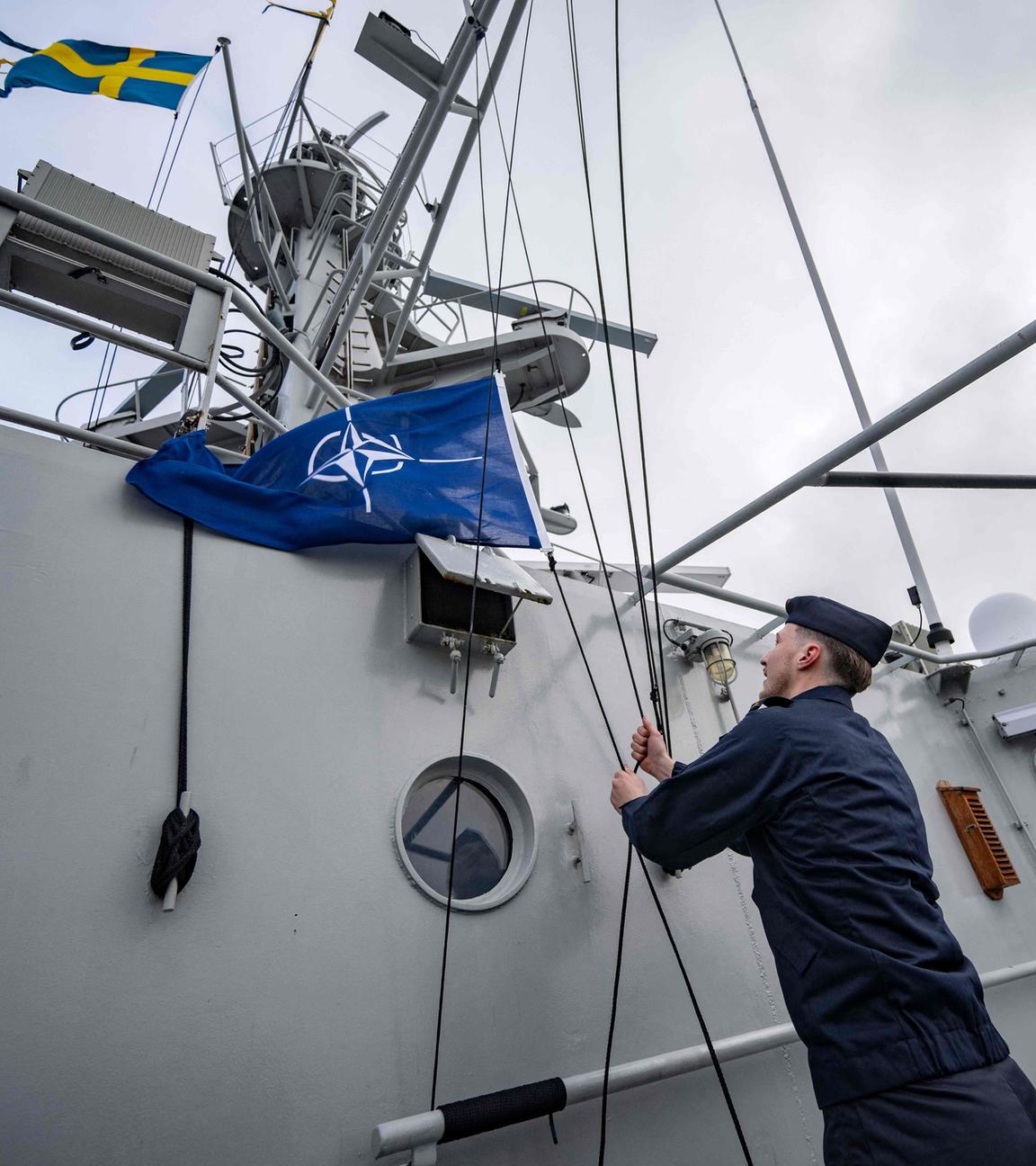 Das Bild zeigt den Kommandanten des Schiffs wie er den Befehl gibt, die NATO-Flagge auf dem Patrouillenschiff zu hissen.