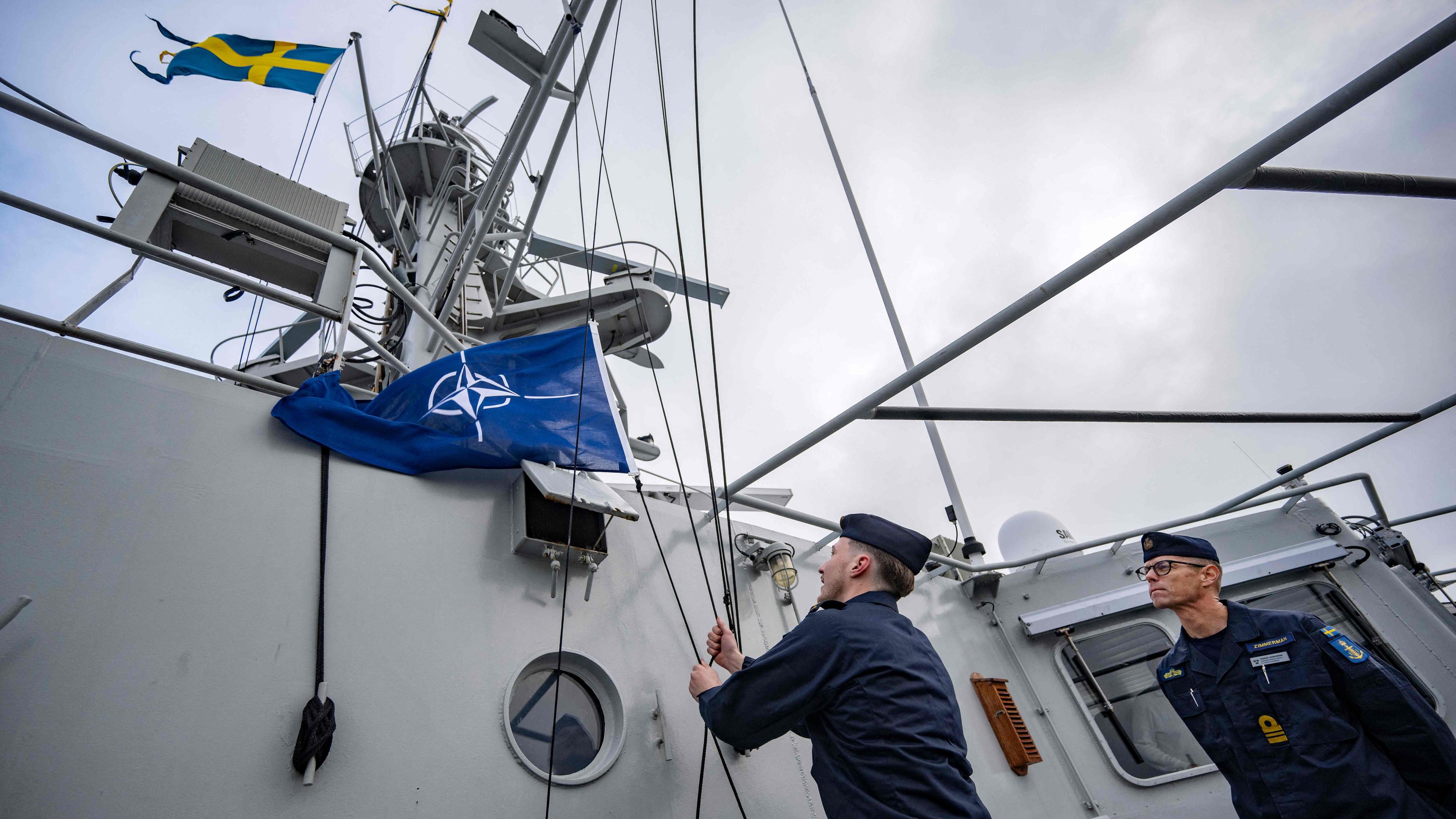 Das Bild zeigt den Kommandanten des Schiffs wie er den Befehl gibt, die NATO-Flagge auf dem Patrouillenschiff zu hissen.