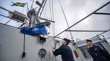 Das Bild zeigt den Kommandanten des Schiffs wie er den Befehl gibt, die NATO-Flagge auf dem Patrouillenschiff zu hissen.