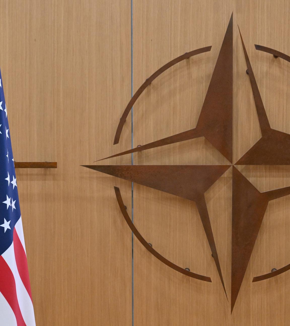 Eine amerikanische Flagge steht links. Das Emblem der Nato ist an der hölzernen Wand zu sehen.