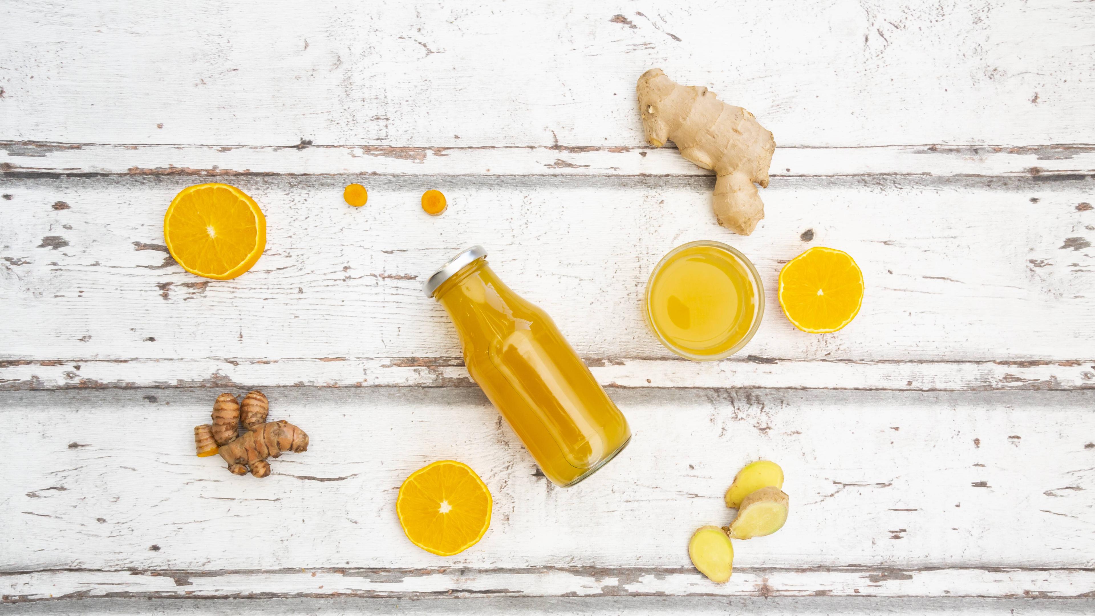 Ingwer, Orangen und zwei Flaschen mit Saft liegen auf einem Tisch.