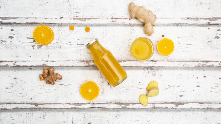 Ingwer, Orangen und zwei Flaschen mit Saft liegen auf einem Tisch.