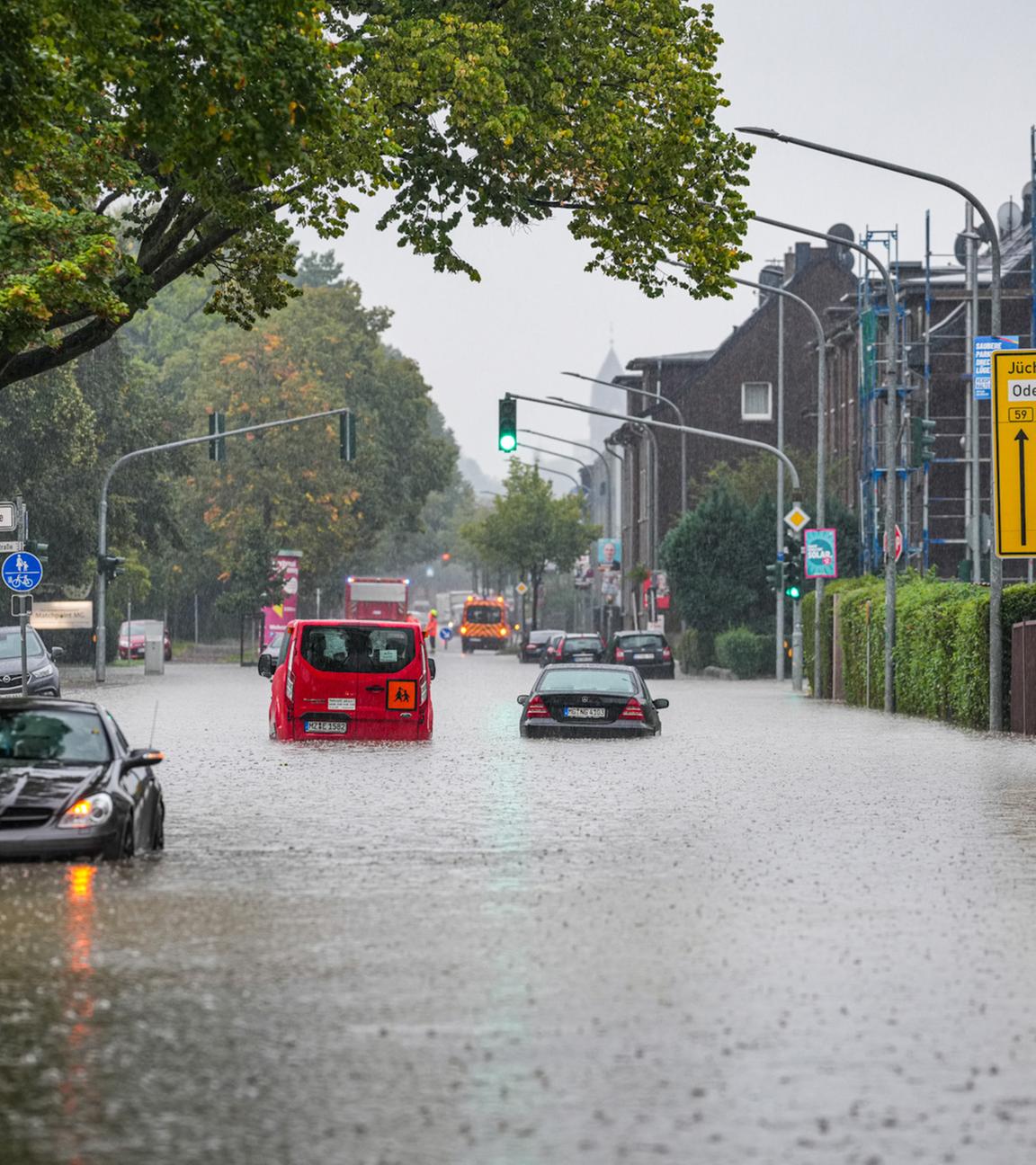Autos fahren bei starkem Regen durch eine überflutete Straße.
