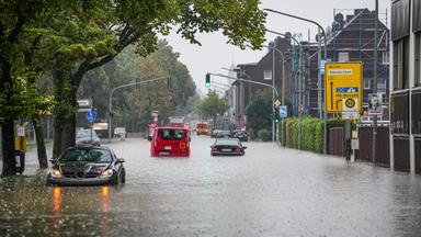 Autos fahren bei starkem Regen durch eine überflutete Straße.
