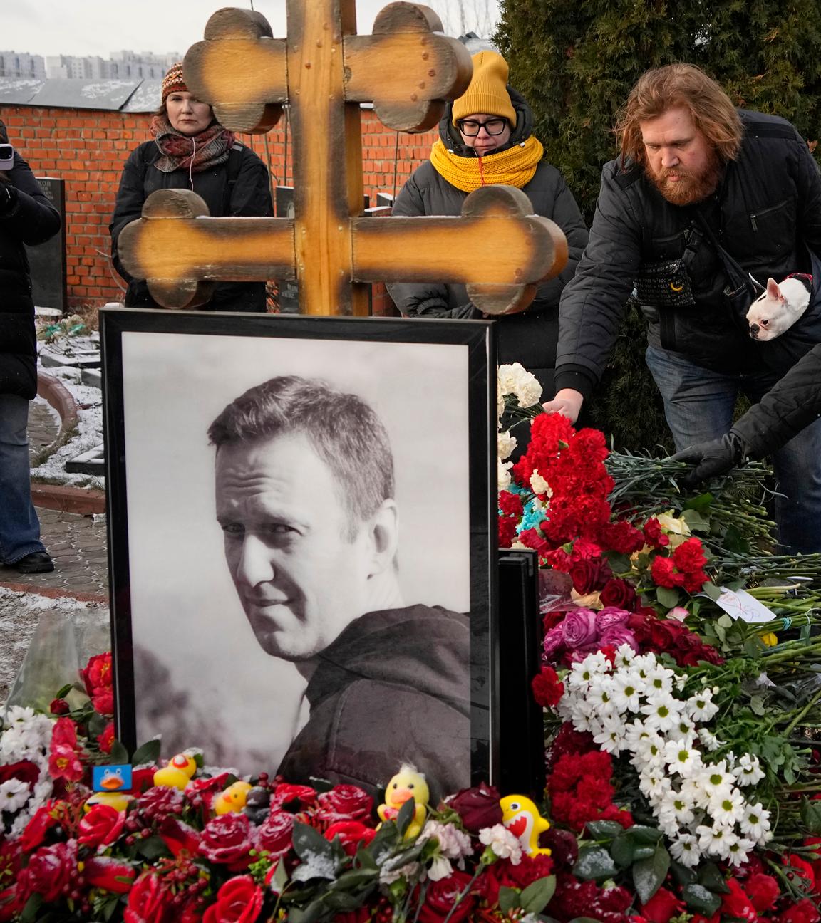 Menschen legen auf einem Friedhof Blumen nieder.