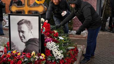 Menschen legen auf einem Friedhof Blumen nieder.