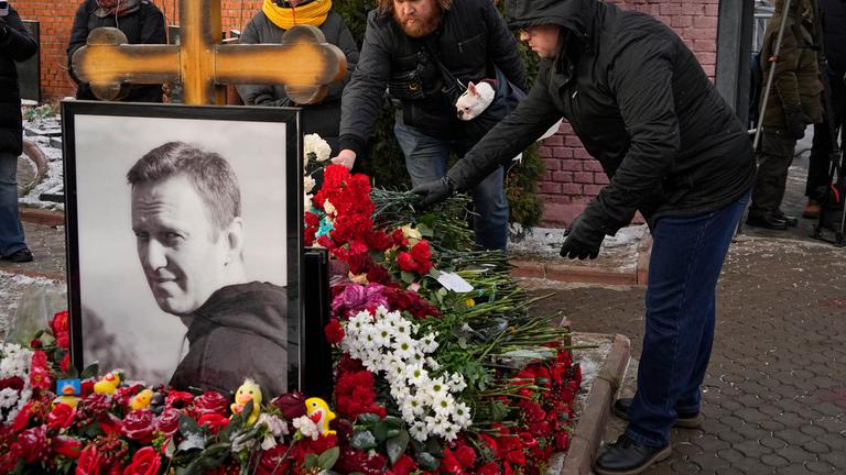 Menschen legen auf einem Friedhof Blumen nieder.