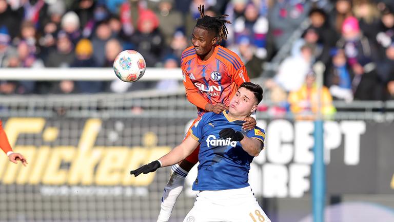 Schalkes linker Verteidiger Moussa Ndiaye springt im Zweikampf mit Kiels Stürmer auf dessen Schulter