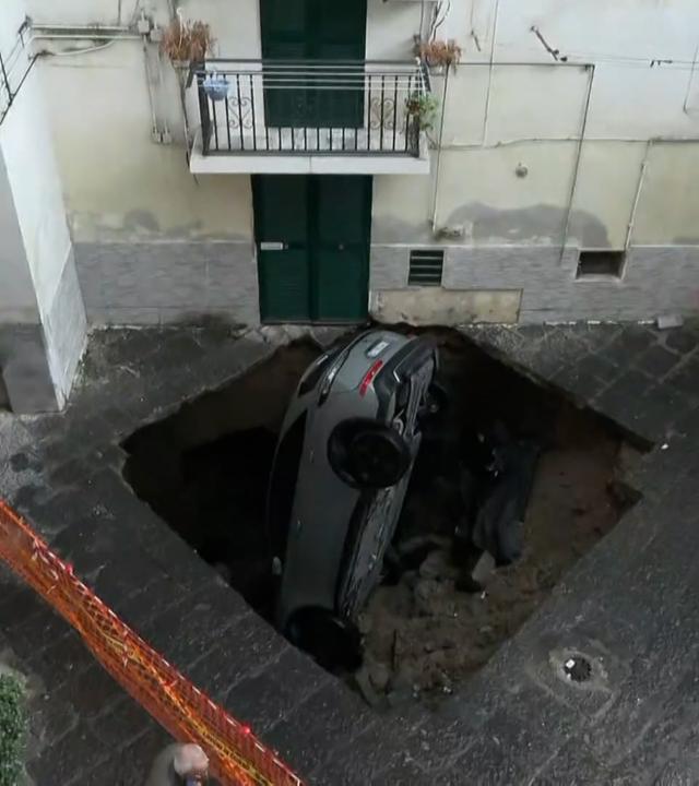 Ein Auto wird von einem riesigen Erdloch verschluckt. Nur noch das Heck ragt raus.