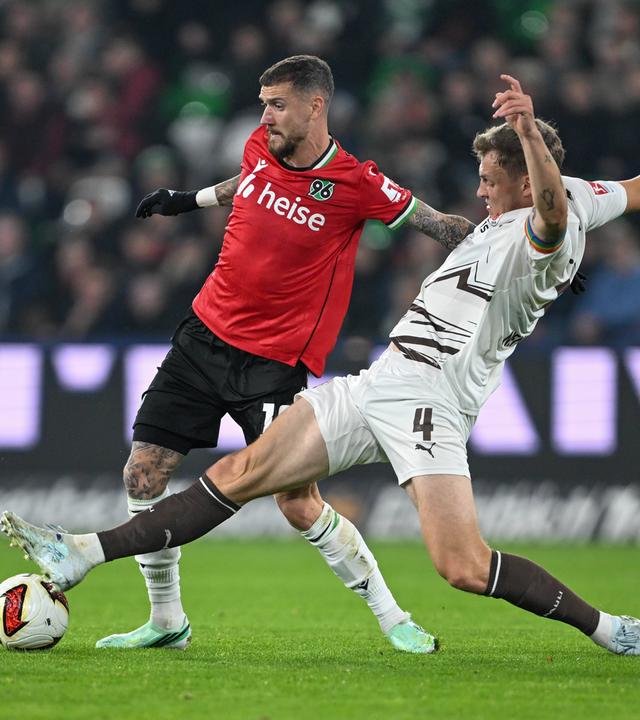 St. Paulis Innenverteidiger David Nemeth grätscht in den Lauf seines Gegenspielers Marcel Hartel von Hannover 96.
