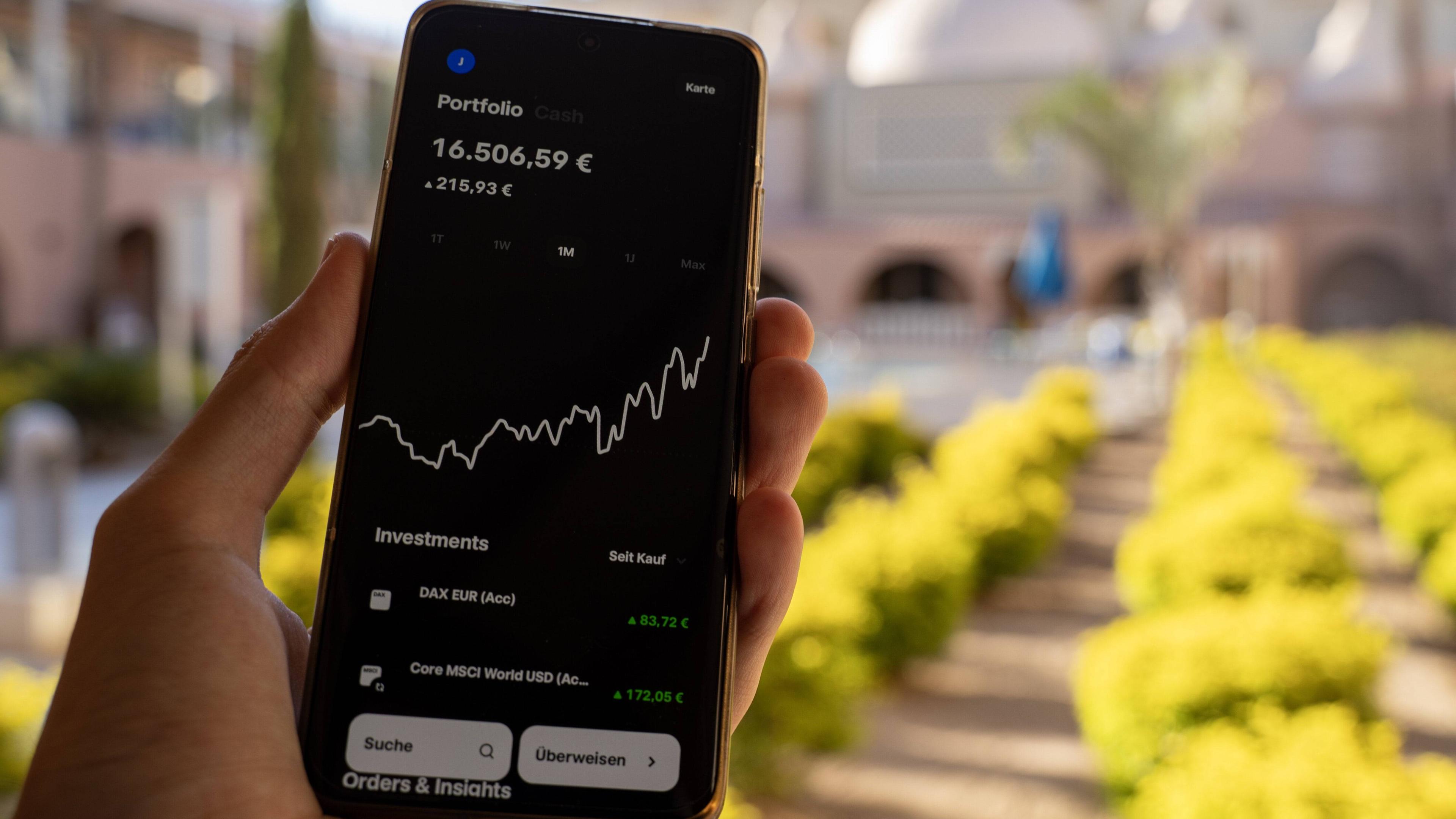 Eine Hand hält ein Smartphone, auf dem einen App für den Aktienhandel geöffnet ist und den Aktienkurs anzeigt.