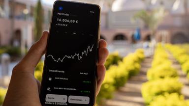 Eine Hand hält ein Smartphone, auf dem einen App für den Aktienhandel geöffnet ist und den Aktienkurs anzeigt.