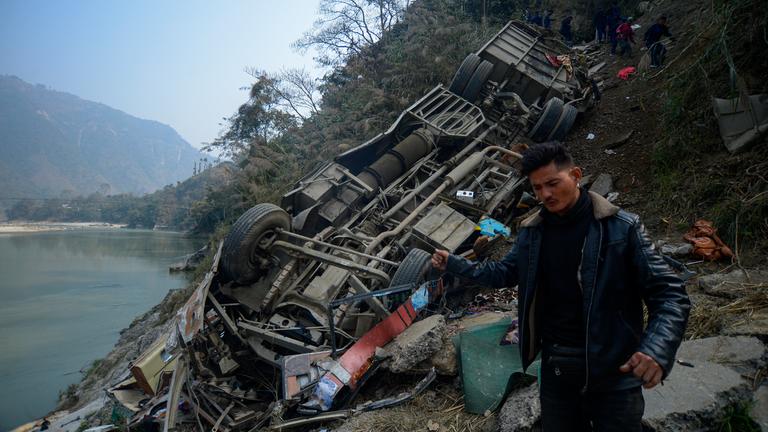 Ein Mann steht vor der Unglücksstelle. Der verunglückte Bus liegt auf dem Dach am Hang, weiter unten ist ein See.